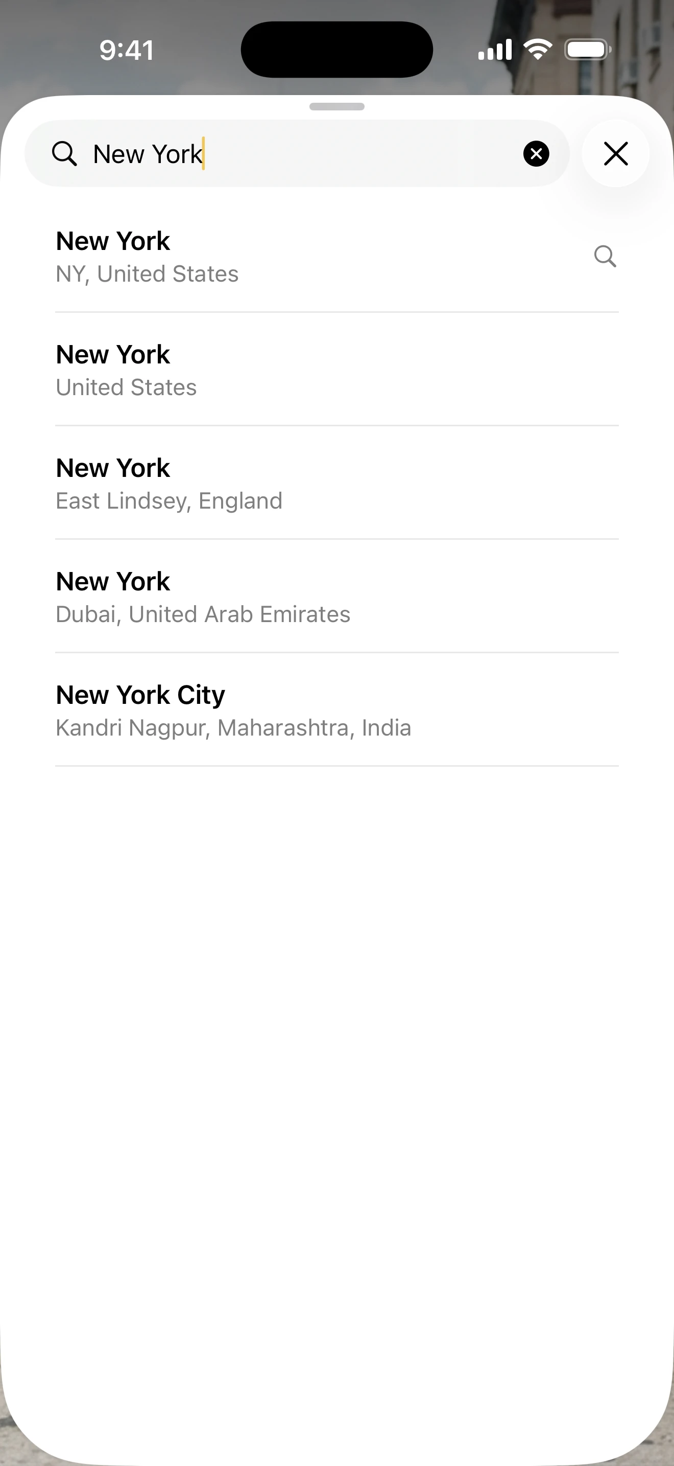 iOS search sheet: typing “New York” returns disambiguated results — NY, England, Dubai, India.